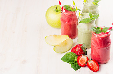 Freshly blended green and red fruit smoothie  in glass jars with straw, mint leafs of strawberry and apples. White wooden board background, copy space.