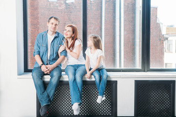 Happy family mother father child portrait sitting on window sill