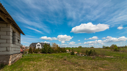Spring-summer rural landscape. View of the cottages under a beautiful cloudy sky with an unfinished house in the foreground