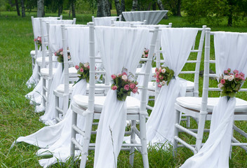 White chairs stand in the rows before wedding altar with flowers in park
