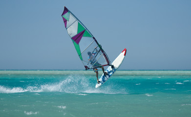 Recreational water sports: windsurfing. Windsurfer surfing waves and jumping high in the sea on a windy day. Extreme sports action with wind and water. Recreational sporting activity