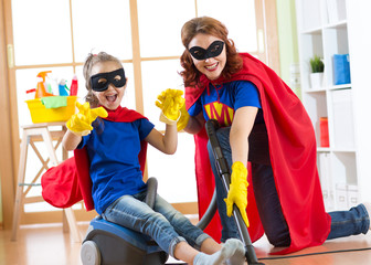 Kid girl and her mother weared Superhero costumes. Cute helper child and woman make cleaning room and have a fun.