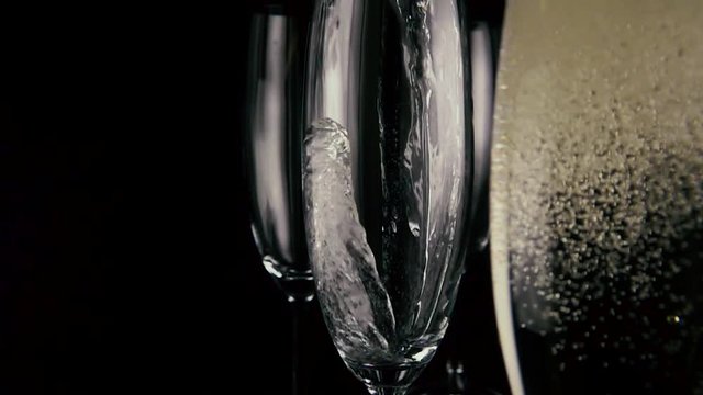 Slow motion. Champagne is poured into one of three glasses, in the foreground a glass of champagne