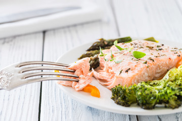 Baked salmon with vegetables on plate. White wooden table