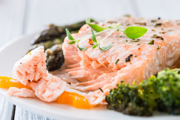 Baked salmon with vegetables on plate. White wooden table