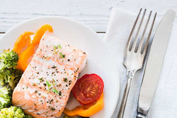 Baked salmon with vegetables on plate. White wooden table