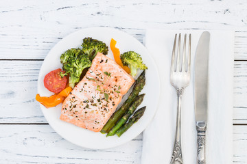 Baked salmon with vegetables on plate. White wooden table