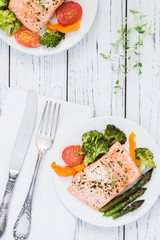 Baked salmon with vegetables on plate. White wooden table