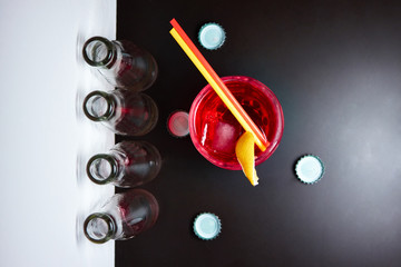 Negroni red cocktail with a slice of lemon with two tubes of red and yellow on a black background, around the empty bottles and caps. Top view/view from above