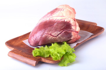 Raw beef heart and lettuce leaf on wooden desk isolated on white background from above and copy space. ready for cooking.