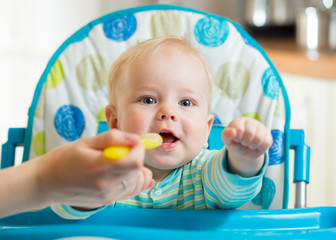 family and nutrition concept - mother spoon feeding little baby sitting in highchair at home