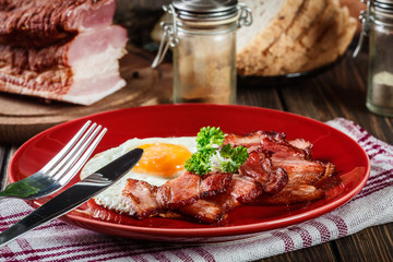 Slices of smoked bacon and fried egg on a red plate