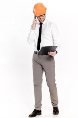 Young construction engineer in orange helmet with folder talking on phone on white background