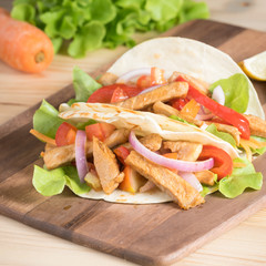 Grilled meat with onion and bell peppers, tomato,lettuce and serve with flour tortilla on wooden board.