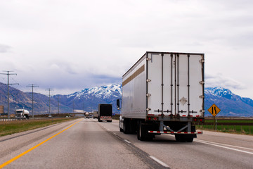 Picturesque straight highway trucks trailers snow capped mountains of Utah