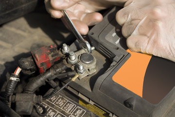 Dłonie mechanika samochodowego w rękawiczkach jednorazowych odkręcają klemę akumulatora. Klema akumulatora odkręcana przez serwisanta. Naprawa samochodu w warsztacie. Odłączanie akumulatora.