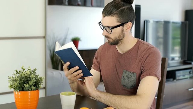 Handsome man reading book in his flat and having painful headache, steadycam shot
