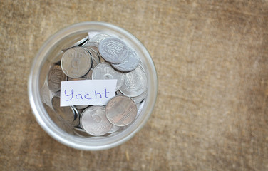 Glass jar filled with coins labeled with the words of the yacht. View from above. Background of burlap. The concept of saving money. Accumulating finances
