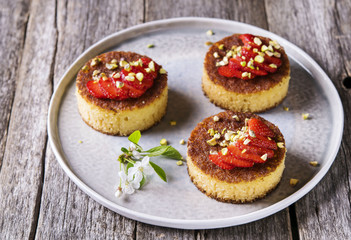 Pieces of homemade sponge cake with strawberry and pistachio decorated flowers of cherry on a rustic vintage wooden table. Selective focus 