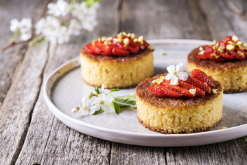 Pieces of homemade sponge cake with strawberry and pistachio decorated flowers of cherry on a rustic vintage wooden table. Selective focus 