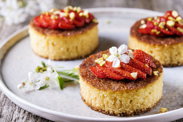 Pieces of homemade sponge cake with strawberry and pistachio decorated flowers of cherry on a rustic vintage wooden table. Selective focus 