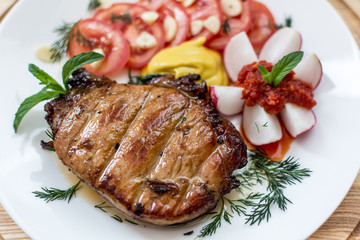 Steak with vegetables, dill and garlic greens, decorated with mint with mustard and ajika on a white plate close-up, shallow depth of field