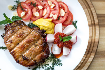 Steak with vegetables, dill and garlic greens, decorated with mint with mustard and ajika on a white plate close-up, shallow depth of field