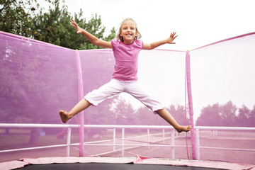 Happy caucasian girl jumping high on a trampoline on a sunny day outdoors.