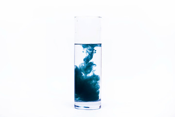 Blue paint falls in a glass with water