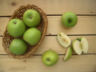 Green sweet apples in a basket and one cut