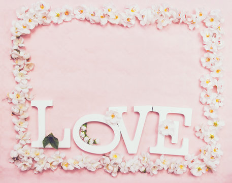 Palabra "love" con un marco de flores sobre fondo rosa 
