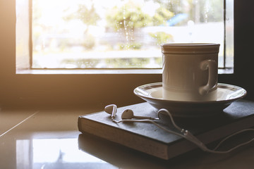 Cup of coffee on book by the window on a rainy day with soft-focus in the background. over light