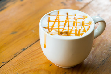 Hot Macchiato coffee with caramel in white cup on wood table