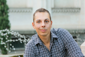 Young man smile on a summer day. Man sitting on the stone fountain. Portrait attractive boy