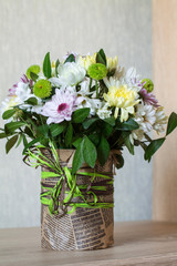 Bouquet of different chrysanthemums in paper with bow on wood.