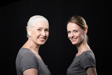 smiling women looking at camera, young and senior people isolated on black