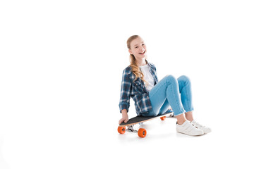 happy girl sitting on skateboard isolated on white in studio