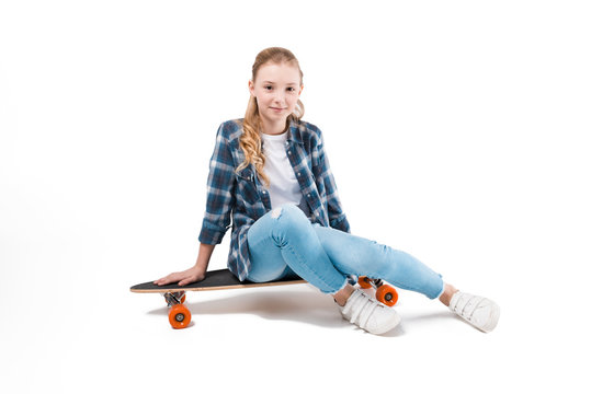 happy girl sitting on skateboard isolated on white in studio