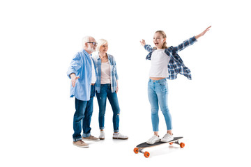 Obraz premium grandfather, grandmother and happy granddaughter with skateboard isolated on white