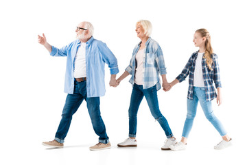 happy grandfather, grandmother and granddaughter walking and holding hands together isolated on white