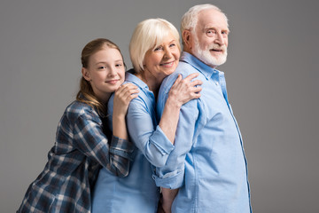 happy family hugging and looking at camera isolated on grey in studio