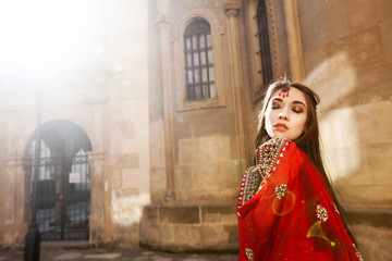 Indian bride raises her red sari up posing in the rays of morning light