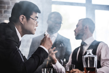 Multiethnic group of businessmen smoking and drinking whisky indoors, business team meeting