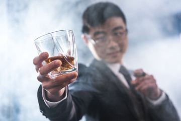 Close-up view of confident asian businessman drinking whiskey and smoking cigar