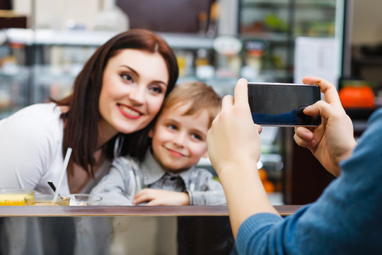 A man makes picture of young mother with her little son at a table in a cafe