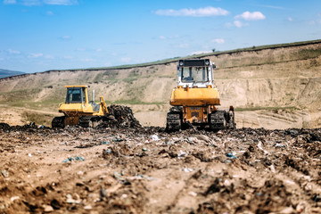 Obraz premium Yellow mini bulldozers working and moving garbage on dumping site