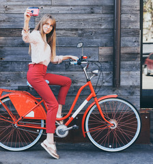 Pretty smiling young woman using taking self portrait on pink vintage camera with retro bicycle...