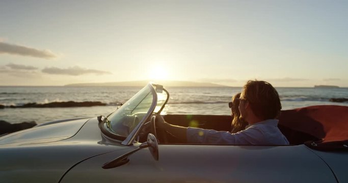 Romantic Couple Hands in thr Air Driving in Vintage Convertible Car at Sunset on Country Road by the Sea