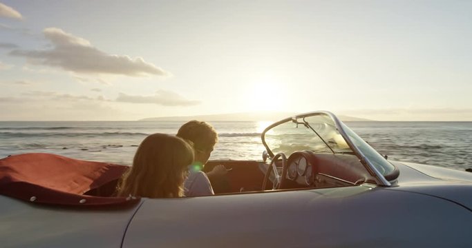 Romantic Couple Hands in thr Air Driving in Vintage Convertible Car at Sunset on Country Road by the Sea