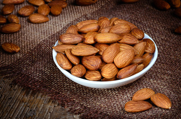 Almonds in a bowl on textured wooden background. Organic food.